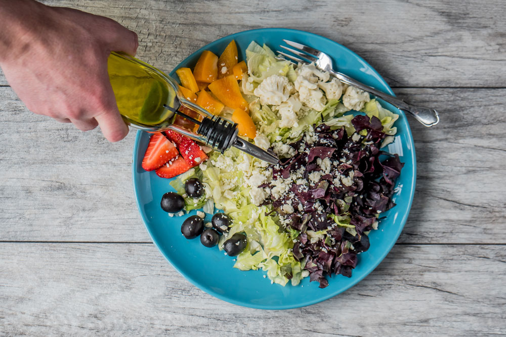 prato com salada de vegetais com mão de uma pessoa colocando azeite de oliva no prato, imagem vista de cima